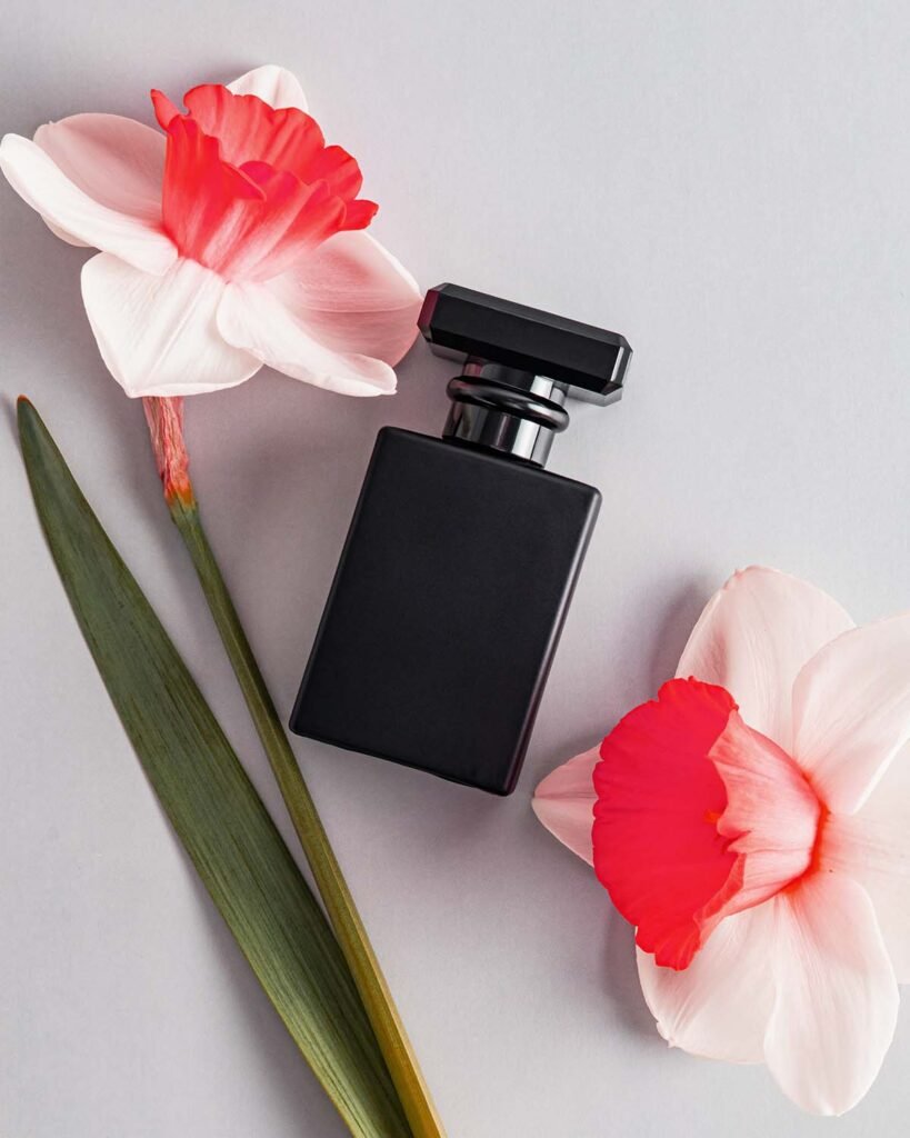 Matte black men's perfume bottle on a light vertical background with a delicate narcissus flower. Template for perfume or eau de toilette. Top view